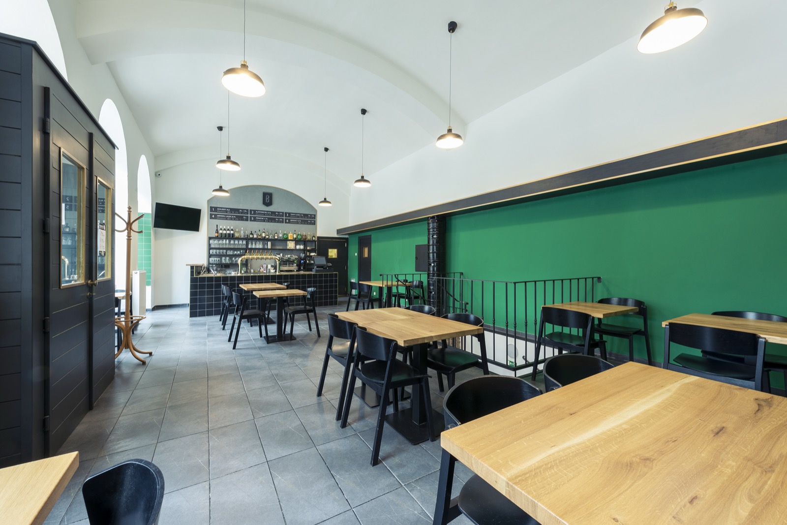 The bright room of Pivovarský klub in Karlín, with wooden tables and the bar behind.